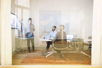 Businesswoman giving presentation to colleagues seen through window