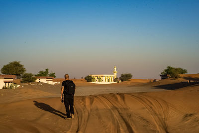 Man riding bicycle on desert against clear sky