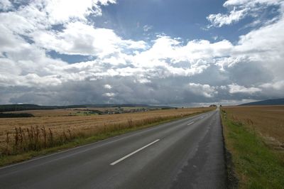 Road passing through field against cloudy sky