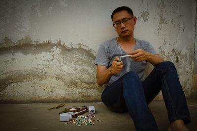 Man holding marijuana joint while sitting against wall