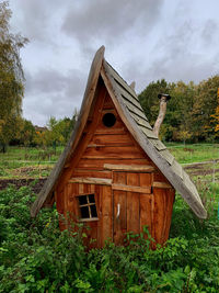 Old wooden house on field by trees against sky