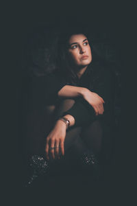 Portrait of young woman sitting against black background