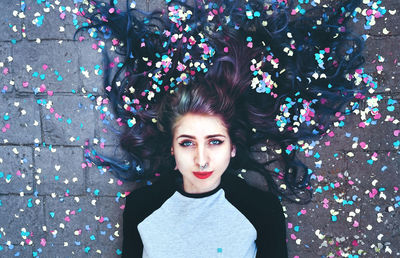 Directly above portrait of woman lying with colorful confetti on footpath