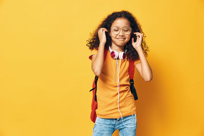 Young woman standing against yellow background