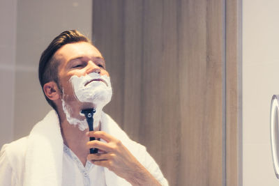 Man using razor while shaving in bathroom