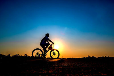 Low angle view of man riding bicycle on street against sky during sunset