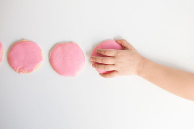 Overhead view of child's hand taking pink frosted sugar cookie