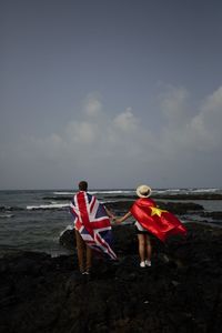 Rear view of couple on beach against sky with uk and vietnam flags