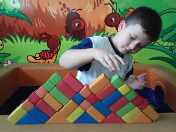 Cute boy playing with colorful toy blocks on table at home