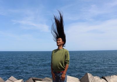 Portrait of smiling young woman standing by sea against sky