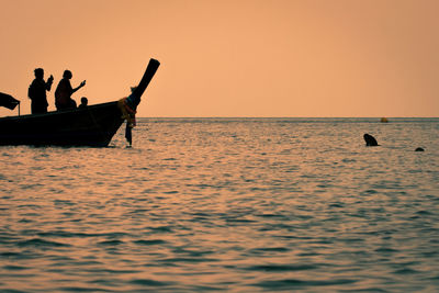 Silhouette people in sea against sky during sunset