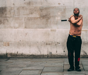 Full length of shirtless man standing against wall