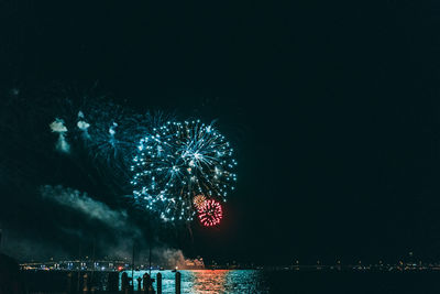 Illuminated firework display over river against sky at night