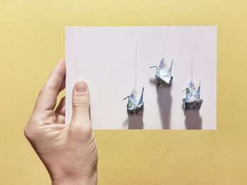 Close-up of person hand holding origami on paper over yellow background