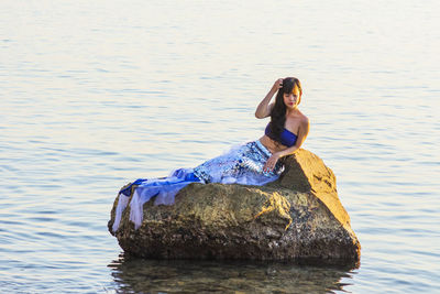 Young woman sitting on rock by lake