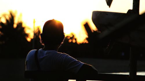 Rear view of man standing by railing during sunset