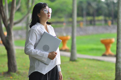 Young woman looking away while standing on field