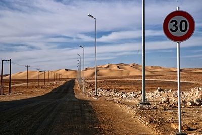 Road sign on street against sky