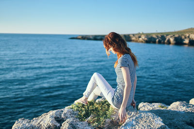 Woman sitting on rock by sea against sky