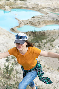 Happy young smiling woman in cap running on sand of clay quarry with blue turquoise water, landscape