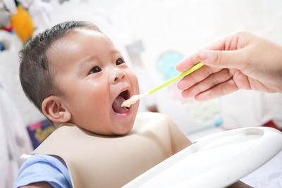 A happy asian baby boy sitting and feeding some pap pudding by mom with spoon.