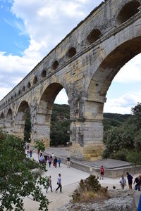 People at bridge against cloudy sky