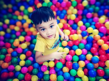 Portrait of cute boy standing amidst multi colored balls