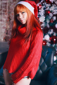 Portrait of sensuous woman wearing red sweater and santa hat standing against christmas tree