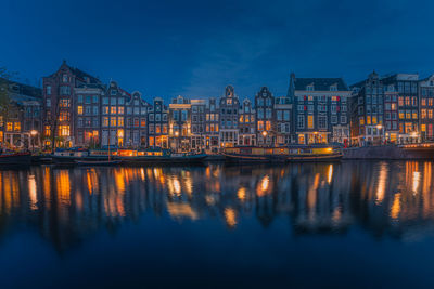 Illuminated buildings by river against sky at night