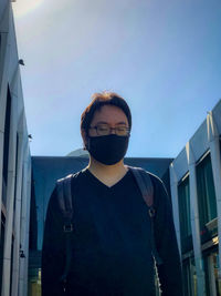 Portrait of young man standing against sky and buildings.