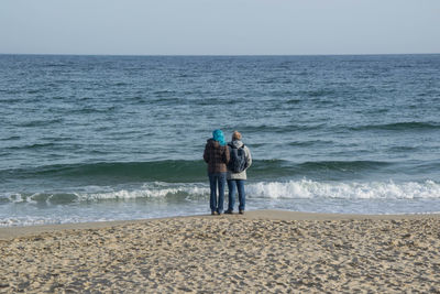 Rear view of men standing at beach against sky