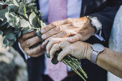 Cropped image of newlywed couple showing rings while holding bouquet during wedding ceremony