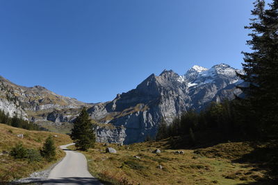 Road leading towards mountains against clear blue sky