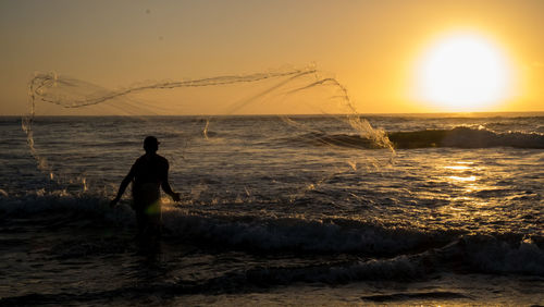 Silhouette man on sea against sky during sunset