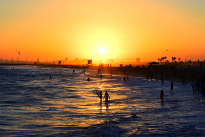 Silhouette people on beach against sky during sunset