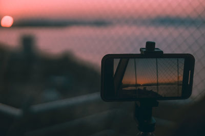 Close-up of smartphone photographing against sky at sunset