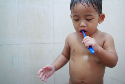 Close-up of shirtless boy holding toothbrush in bathroom