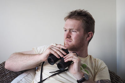 Portrait of young man holding camera against wall