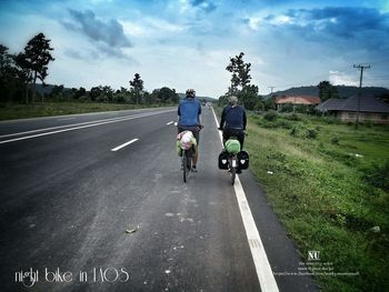 Rear view of people riding motorcycle on road against sky