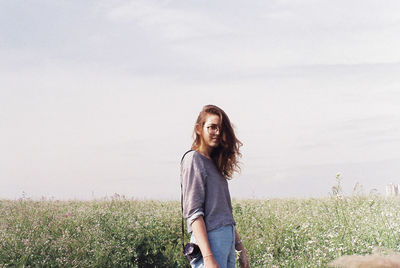 Portrait of smiling young woman standing on field against sky