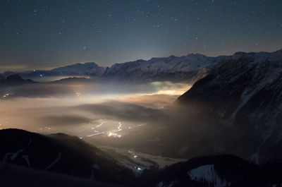 Scenic view of illuminated town covered with fog amidst snowcapped mountains