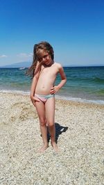 Full length of cute girl standing at beach against blue sky on sunny day