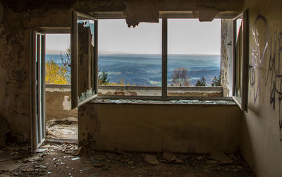 Abandoned building by sea against sky seen through window