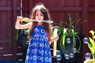 Girl blowing bubbles while standing against fence