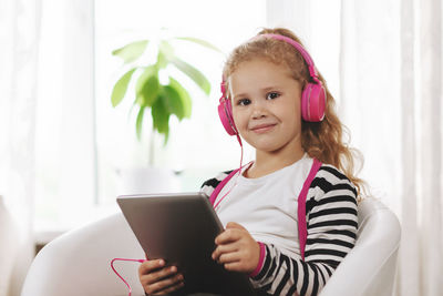 A school girl in pink headphones sits with a tablet and listens to an online lesson.online education
