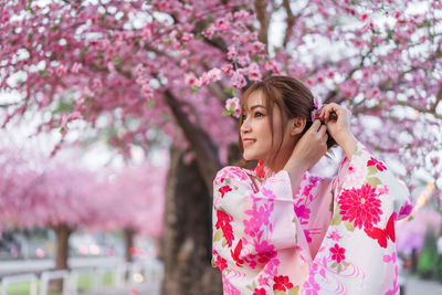 Woman standing by pink cherry blossom tree