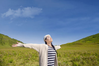 Woman standing with arms outstretched on field against sky