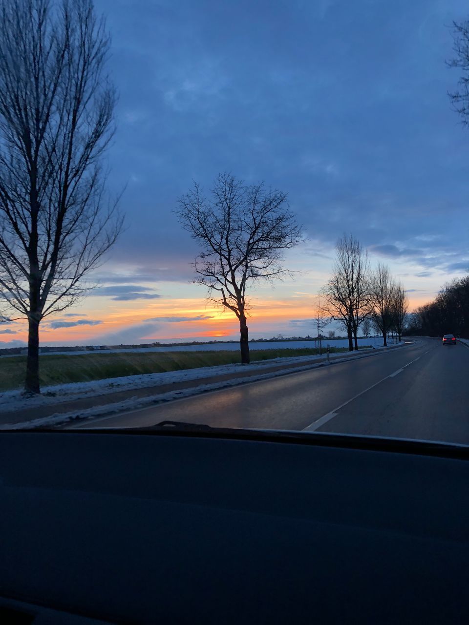 BARE TREES BY ROAD AGAINST SKY AT SUNSET