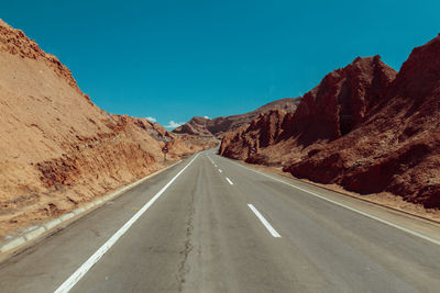 Empty road amidst mountains against clear sky