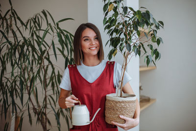 Smiling young woman holding a watering can and a homemade green plant in a pot